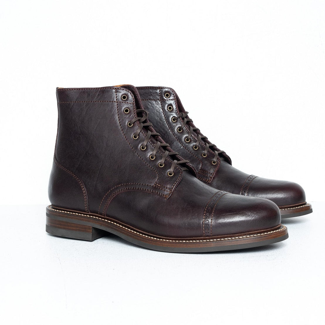 A pair of dark brown leather lace-up ankle boots with a cap toe and stacked heels, photographed on a clean white studio surface.